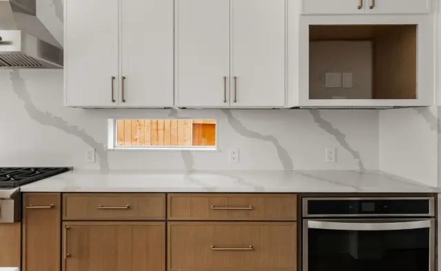 Black Gold Bend Residence: White uppers + rift-cut oak lowers/island, dramatic veined quartz counters and backsplash, glass-front uppers, black refrigerator, brushed-gold hardware — view 5