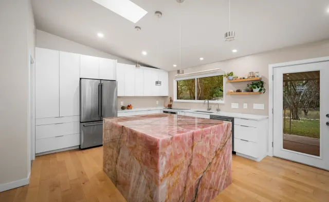 Cupid Residence: White flat-panel handleless cabinetry, rose-quartz waterfall island focal point, integrated lighting, floor-to-ceiling storage under vaulted ceiling — view 2