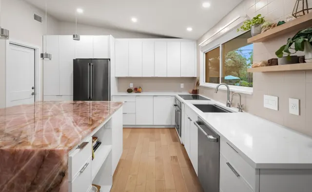 Cupid Residence: White flat-panel handleless cabinetry, rose-quartz waterfall island focal point, integrated lighting, floor-to-ceiling storage under vaulted ceiling — view 3