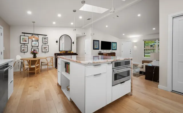 Cupid Residence: White flat-panel handleless cabinetry, rose-quartz waterfall island focal point, integrated lighting, floor-to-ceiling storage under vaulted ceiling — view 4
