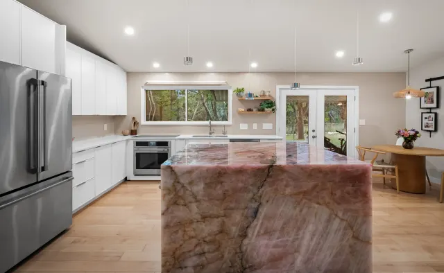 Cupid Residence: White flat-panel handleless cabinetry, rose-quartz waterfall island focal point, integrated lighting, floor-to-ceiling storage under vaulted ceiling — view 5