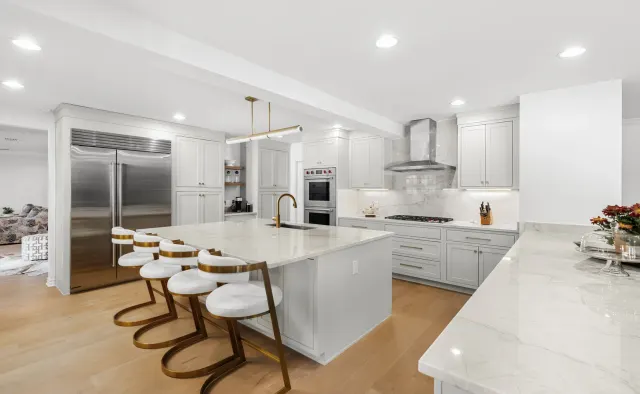 Eastledge Residence: Dove-gray shaker, marble island + backsplash, brass fixtures and barstools, warm wood floors — view 1