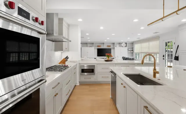 Eastledge Residence: Dove-gray shaker, marble island + backsplash, brass fixtures and barstools, warm wood floors — view 4