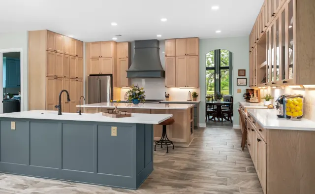 Island Oaks Residence: Natural maple perimeter + slate-blue island, floor-to-ceiling storage, glass-front uppers, custom plaster range hood — view 1