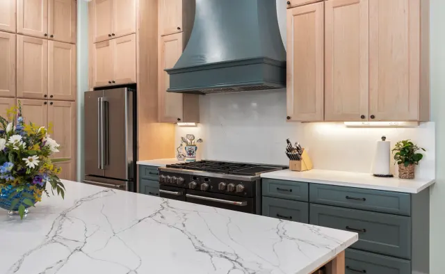 Island Oaks Residence: Natural maple perimeter + slate-blue island, floor-to-ceiling storage, glass-front uppers, custom plaster range hood — view 2