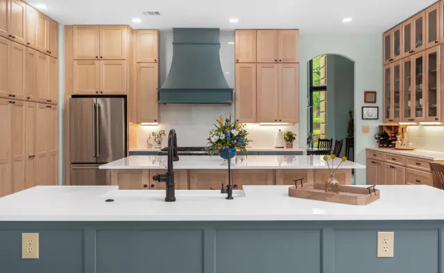 Island Oaks Residence: Natural maple perimeter + slate-blue island, floor-to-ceiling storage, glass-front uppers, custom plaster range hood — view 3
