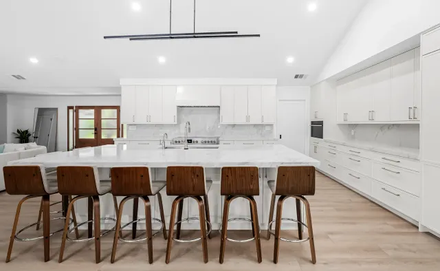 McNeil Dr Residence: White shaker under vaulted ceiling, marble island seating six, full marble backsplash, waterfall edges, walnut barstools — view 1