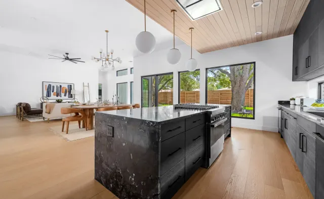 Southern Oaks Residence: Matte-black perimeter, fluted-wood island base, waterfall veined black stone island, reeded wood ceiling, brass accents — view 2