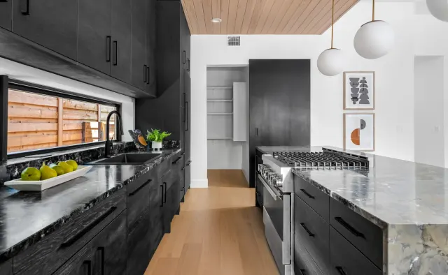 Southern Oaks Residence: Matte-black perimeter, fluted-wood island base, waterfall veined black stone island, reeded wood ceiling, brass accents — view 4