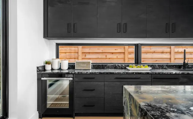 Southern Oaks Residence: Matte-black perimeter, fluted-wood island base, waterfall veined black stone island, reeded wood ceiling, brass accents — view 5